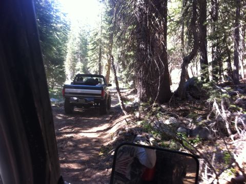 1990 Ford Bronco - A dark blue Ford Bronco navigates a wooded trail, with another vehicle following closely behind.