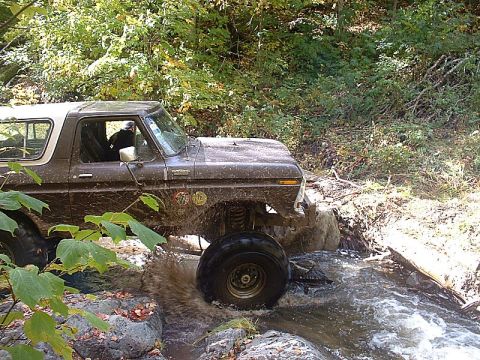 1978 Ford Bronco - A brown 1978 Ford Bronco navigates a rocky stream bed, kicking up water as it goes.