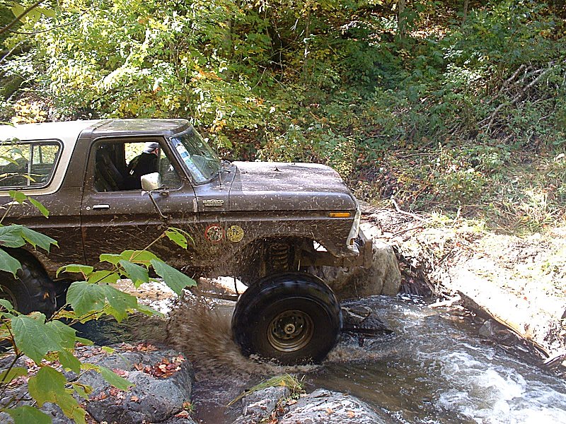 Brown 1978 Ford Bronco driving through water and rocks