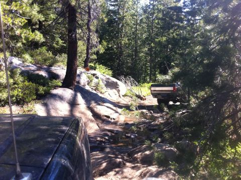 1990 Ford Bronco - Two vehicles are shown traversing a challenging, rocky path through a dense forest.