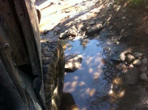 1990 Ford Bronco - A vehicle navigates a rocky, muddy trail with a reflective puddle.