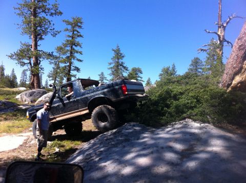 1990 Ford Bronco - A dark blue 1990 Ford Bronco navigates a challenging rocky trail with a person standing nearby.