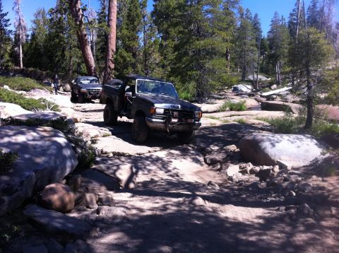 1990 Ford Bronco - Off-roading adventure on a challenging rocky path through a wooded area.