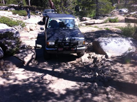 1990 Ford Bronco - A dark 1990 Ford Bronco navigates a challenging rocky trail, with another vehicle visible behind it.