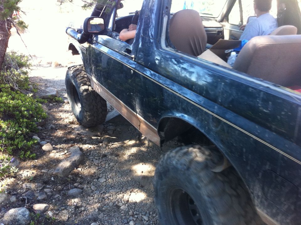 1990 Ford Bronco with lifted suspension and large tires on a rocky, off-road trail