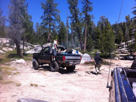 1990 Ford Bronco - A lifted black Ford F-Series truck is parked in a campsite with a tent and another vehicle nearby.