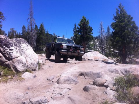 1990 Ford Bronco - 1990 Ford Bronco tackles a challenging off-road course with large rocks and trees.