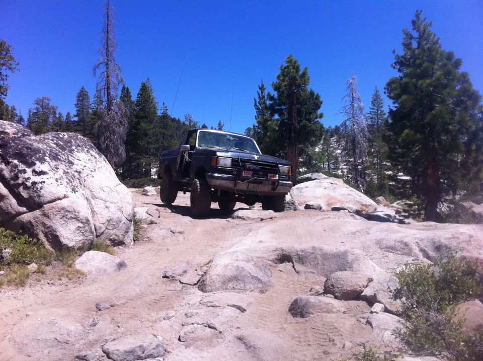 1990 Ford Bronco navigating a boulder-strewn trail under a clear blue sky