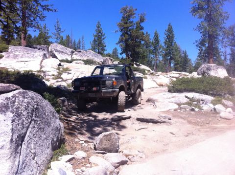 1990 Ford Bronco - 1990 Ford Bronco navigating a challenging rocky path in a wooded area.