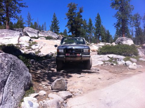 1990 Ford Bronco - A Ford Bronco navigates a rocky, off-road path under a clear blue sky.
