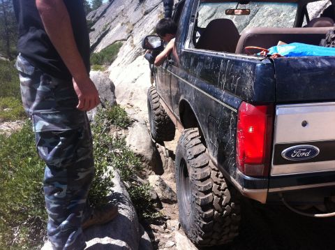 1990 Ford Bronco - A Ford Bronco navigates a challenging rocky trail, its large tires gripping the uneven terrain.