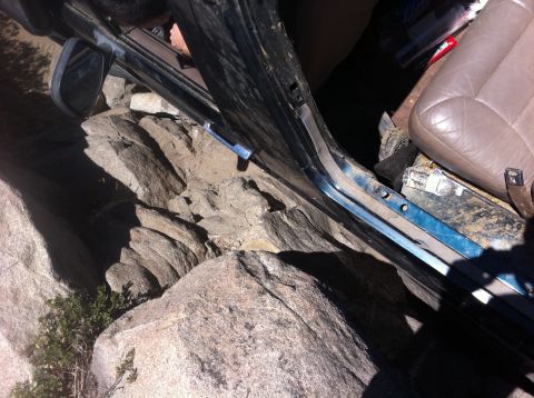 1990 Ford Bronco - The interior of a 1990 Ford Bronco is visible, with the driver's side door open and the vehicle partially lodged in rocks.