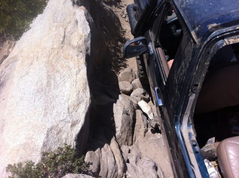1990 Ford Bronco - A black SUV navigates a challenging rocky trail, its door open as it maneuvers through the terrain.