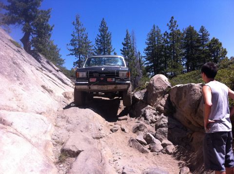1990 Ford Bronco - A black 1990 Ford Bronco tackles a challenging rocky off-road path under a clear blue sky.