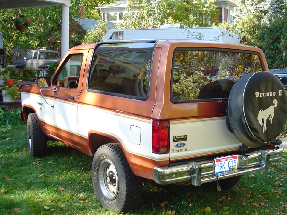 Two-tone orange and white Ford Bronco II from the rear quarter with Bronco II spare tire cover, parked on grass