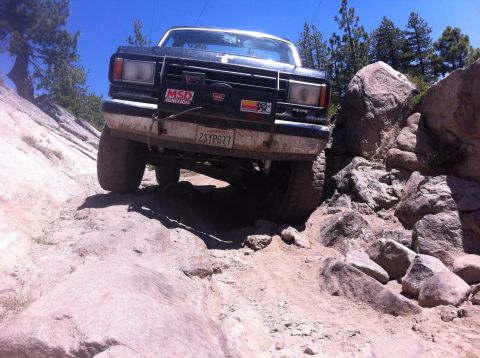 1990 Ford Bronco - A Ford Bronco navigates a challenging rocky trail under a clear blue sky.