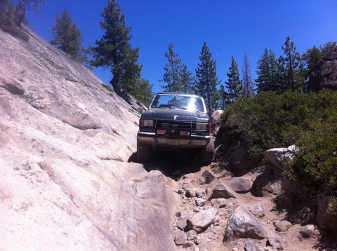 1990 Ford Bronco - This 1990 Ford Bronco navigates a challenging rocky off-road path under a clear blue sky.