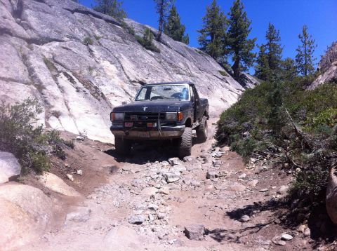 1990 Ford Bronco - Ford pickup truck navigates a challenging rocky trail in a mountainous landscape.
