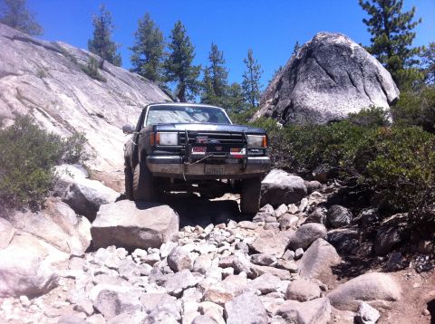 1990 Ford Bronco - A Ford Bronco tackles a challenging rocky terrain under a clear blue sky.