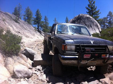 1990 Ford Bronco - This Ford F-Series truck navigates a challenging rocky off-road path under a clear blue sky.