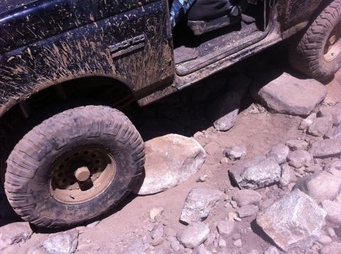 1990 Ford Bronco - A black Ford Bronco navigates a rocky terrain, with mud splattered across its body.