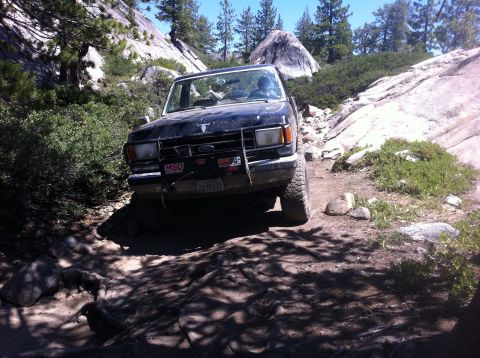 1990 Ford Bronco - This 1990 Ford Bronco is shown tackling a challenging off-road path in a mountainous, wooded area.