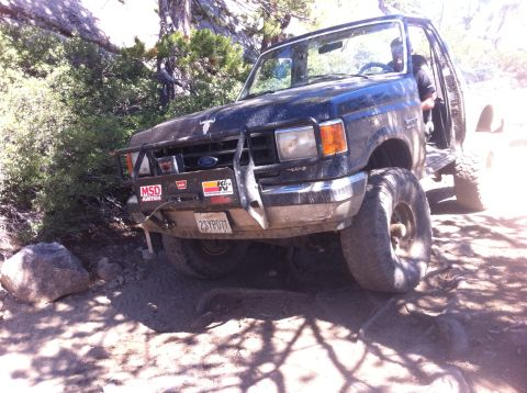 1990 Ford Bronco - This dark-colored Ford Bronco is navigating a rocky, off-road trail with a modified front bumper.