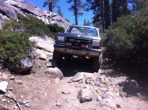 1990 Ford Bronco - This 1990 Ford Bronco tackles a challenging off-road path with large rocks and trees.