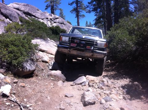 1990 Ford Bronco - 1990 Ford Bronco tackling a challenging rocky trail in a wooded, mountainous area.