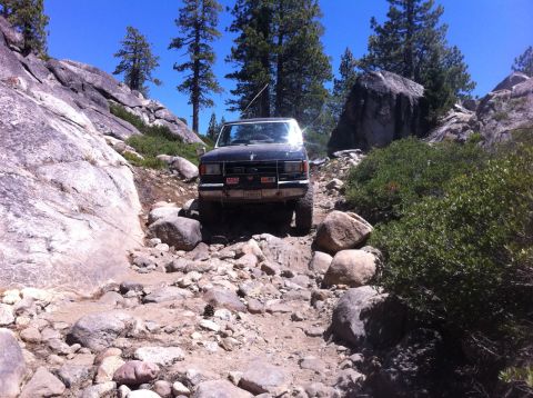 1990 Ford Bronco - A 1990 Ford Bronco tackles a challenging off-road path with large boulders and sparse vegetation.