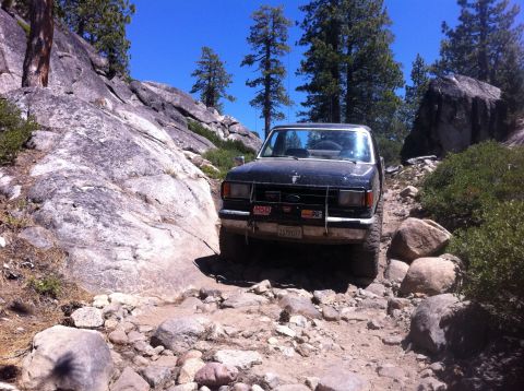 1990 Ford Bronco - Ford Bronco tackling a difficult off-road path with large rocks and trees.