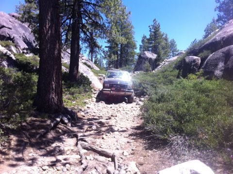 1990 Ford Bronco - A dark SUV navigates a challenging rocky path through a wooded, mountainous area.