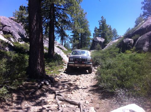 1990 Ford Bronco - A 1990 Ford Bronco navigates a challenging, rocky path through a wooded, mountainous landscape.