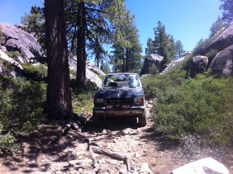 1990 Ford Bronco - 1990 Ford Bronco navigating a rough, off-road trail in a mountainous, wooded area.