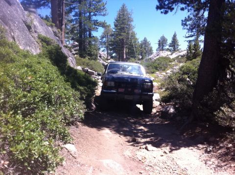 1990 Ford Bronco - Black 1990 Ford Bronco navigates a challenging rocky trail surrounded by trees and boulders.