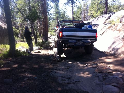 1990 Ford Bronco - 1990 Ford Bronco navigates a challenging rocky path through a wooded area.