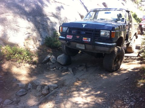 1990 Ford Bronco - This Ford Bronco is tackling a challenging off-road course with large rocks and uneven terrain.