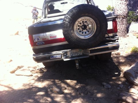 1990 Ford Bronco - A Ford Bronco navigates a rough, rocky terrain under a bright sun.