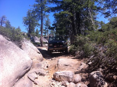 1990 Ford Bronco - A 1990 Ford Bronco tackles a challenging rocky path surrounded by trees and boulders.