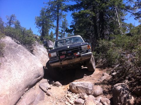 1990 Ford Bronco - This Ford Bronco is tackling a challenging off-road path with significant rock obstacles.