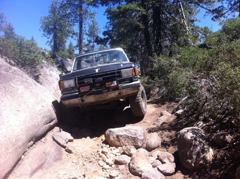 1990 Ford Bronco - This Ford Bronco is tackling a challenging off-road path with large rocks and trees.