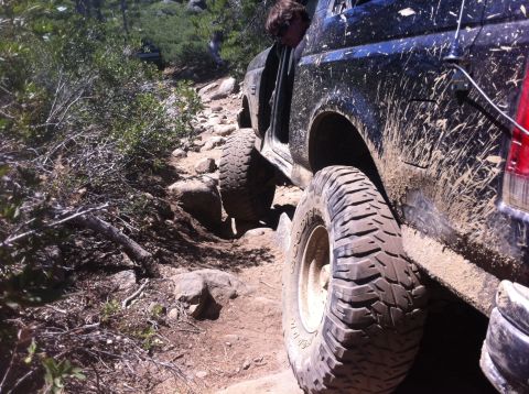 1990 Ford Bronco - A black 1990 Ford Bronco navigates a challenging rocky trail, covered in mud.