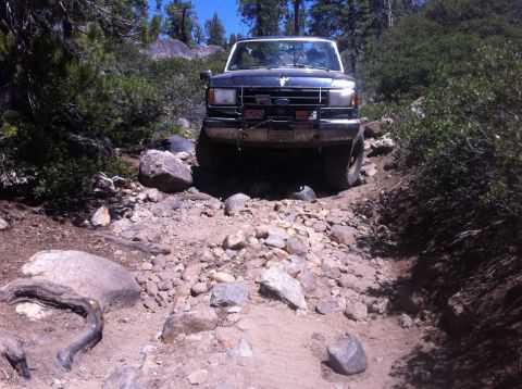 1990 Ford Bronco - Ford Bronco tackling a challenging rocky trail in a wooded area.