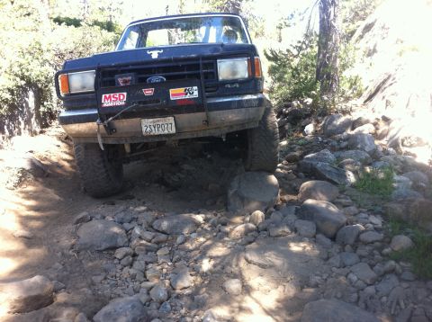 1990 Ford Bronco - This Ford Bronco is tackling a challenging, rocky off-road path in a wooded area.