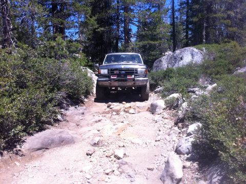 1990 Ford Bronco - 1990 Ford Bronco navigating a rough, rocky trail through a wooded area.