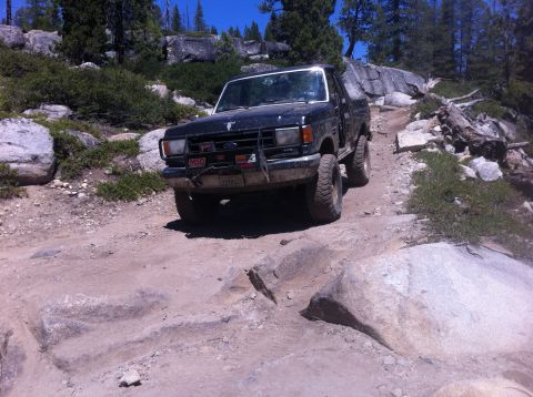 1990 Ford Bronco - Ford Bronco tackling a challenging rocky trail in a wooded, mountainous area.