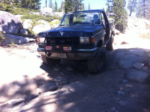 1990 Ford Bronco - This truck is navigating a difficult, rocky trail in a wooded, mountainous area.