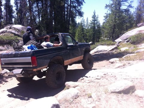 1990 Ford Bronco - Ford Bronco navigates a challenging off-road path with large rocks and trees surrounding it.