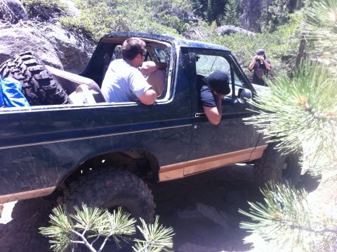 1990 Ford Bronco - A dark green 1980s Ford Bronco navigates a rocky trail with occupants inside.