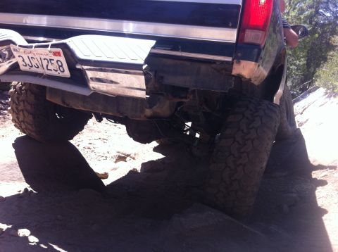 1990 Ford Bronco - The rear of a 1990 Ford Bronco is shown with a damaged bumper while navigating rough, rocky terrain.